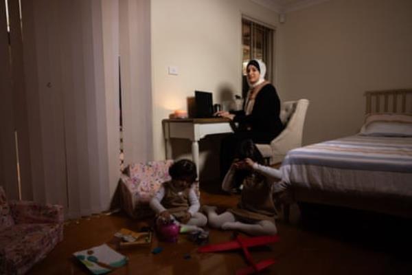 A woman sits on a chair as a child plays on the floor