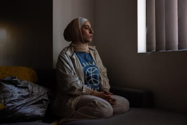 A young woman sits on a bed looking out a window