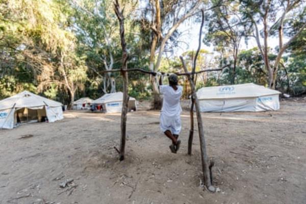 A person exercising on a makeshift stick exercise bar in a tent encampment